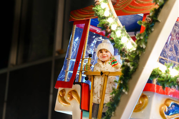 Petite fille d'âge préscolaire chevauchant sur le cheval de carrousel de roue ferris à la foire ou au marché de Noël, en plein air. Happy enfant en bas âge s'amuser sur le marché de Noël familial traditionnel en Allemagne - Photo, image