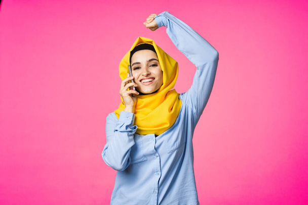 muslim woman in yellow hijab talking on the phone technology pink background - Fotografie, Obrázek