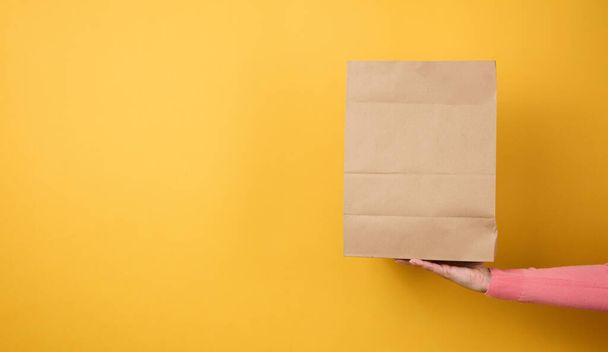 Frau hält braune leere Bastelpapiertüten zum Mitnehmen auf gelbem Hintergrund in der Hand. Verpackungsvorlagen täuschen vor. Lieferservice-Konzept, Banner - Foto, Bild