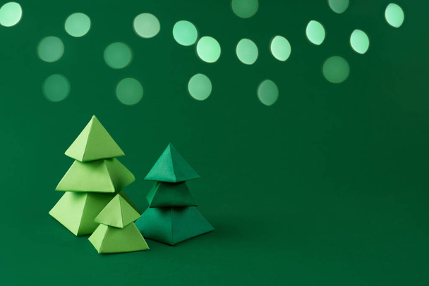 Yeşil arka planda üç yeşil kağıt Noel ağacı. Bokeh ışıkları kağıt işçiliği, Noel konsepti, kopyalama alanı.. - Fotoğraf, Görsel