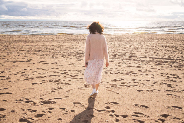 自然と人間の一体性。少女は砂浜に沿って海を歩いている。孤独な少女が海を歩いている。現代人の孤独への恐怖 - 写真・画像