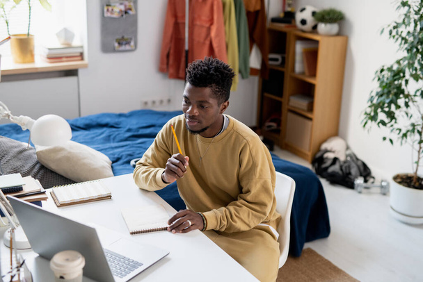Young African student in homewear sitting in front of laptop - 写真・画像