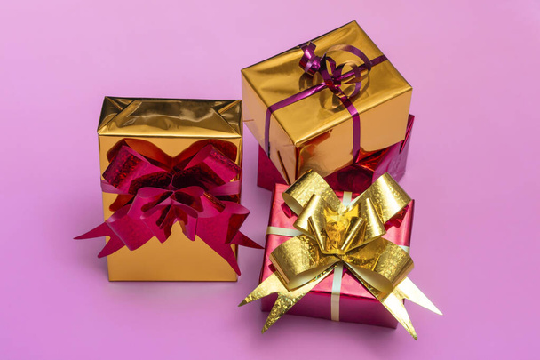 Золотые подарочные коробки с красным бантом на цветном фоне крупным планом, вид сверху - Фото, изображение