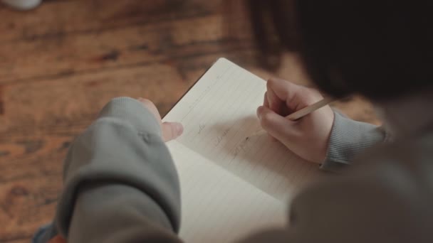 Plan rapproché d'en haut d'une étudiante qui prend des notes dans un cahier à l'intérieur - Séquence, vidéo