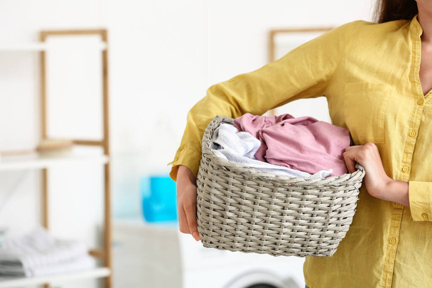 Joven ama de casa sosteniendo cesta de mimbre con lavandería en casa, primer plano - Foto, Imagen