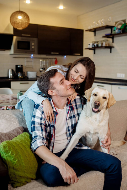 Young couple and their fluffy baby labrador retriever at home in the kitchen - Foto, afbeelding