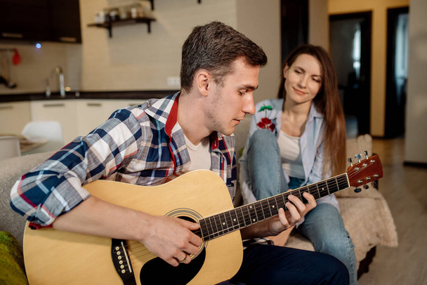 若い男が家でギターを弾き、女性は彼の言うことを聞いて歌います。 - 写真・画像