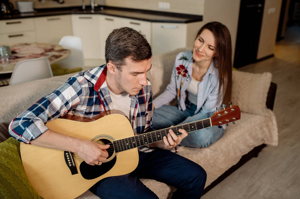 A young man plays the guitar at home, and the woman listens to him and sings - Fotoğraf, Görsel