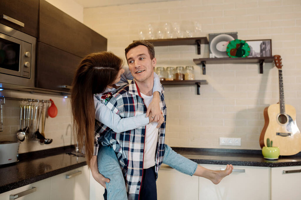 Joven pareja mujer y hombre abrazándose en la cocina en casa, divirtiéndose y sonriendo - Foto, imagen
