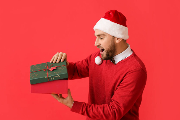 Verrast jongeman opening kerstcadeau op kleur achtergrond - Foto, afbeelding