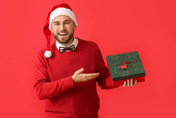 Glücklicher junger Mann mit Weihnachtsgeschenk auf farbigem Hintergrund - Foto, Bild