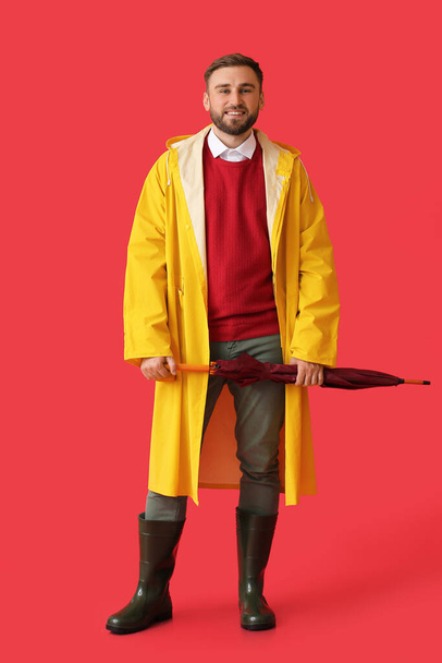 Young man in stylish raincoat and with umbrella on color background - Foto, Bild