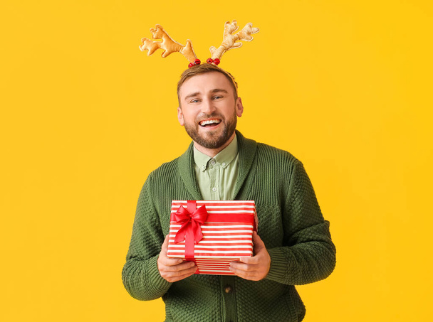 Happy young man with Christmas gift on color background - Photo, Image