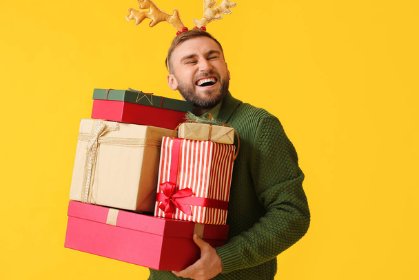 Happy young man with Christmas gifts on color background - Photo, Image