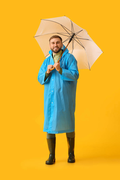 Young man in stylish raincoat and with umbrella on color background - Zdjęcie, obraz
