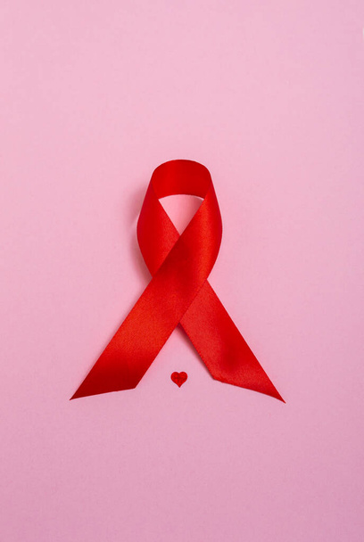 Kızıl AIDS farkındalık kurdelesi ve pembe arka planda bir kalp. Yaklaş, kopyalama alanı. Dikey fotoğraf - Fotoğraf, Görsel