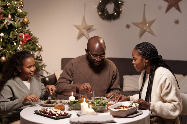 Familia africana feliz de tres interactuando por mesa festiva servida - Foto, imagen