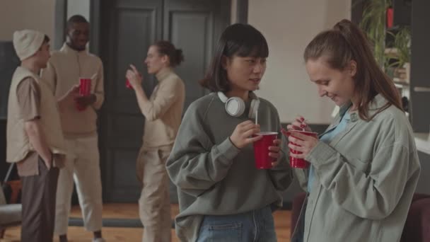 Medium slow mo portret van twee mooie meisjes met wegwerp rode cups chatten op studenten feest op de campus dan zwaaien en glimlachen naar de camera - Video