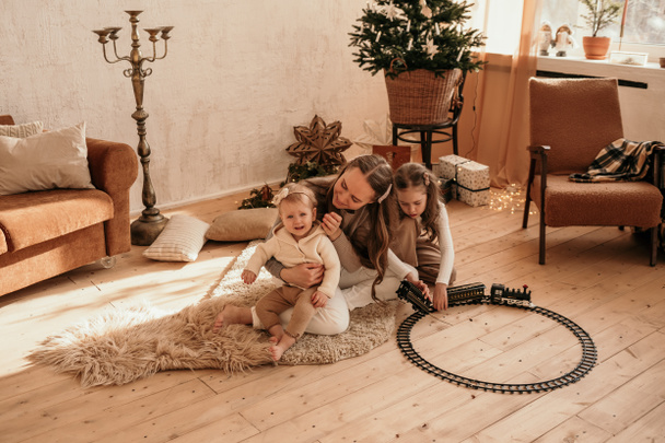 egy gondoskodó anya és lányai ülnek a szőnyegen a szobában, és játszanak a vasúttal és a vonattal. - Fotó, kép