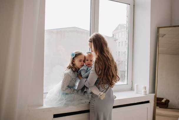 красива мати і її дочки сидять на підвіконні біля вікна в кімнаті з дзеркалом
 - Фото, зображення