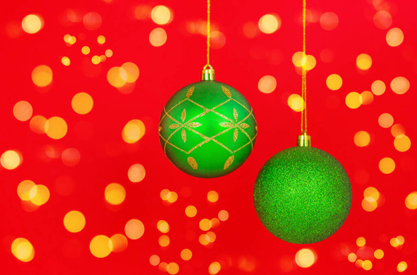 κοντινό πλάνο δύο όμορφων πράσινων χριστουγεννιάτικων μπιχλιμπιδιών σε κόκκινο φόντο με εορταστικά φώτα. - Φωτογραφία, εικόνα