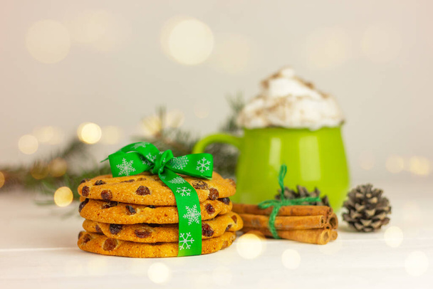 Χριστουγεννιάτικα μπισκότα με πράσινη κορδέλα σε φόντο ξυλάκια κανέλας και κύπελλο. γλυκά διακοπών και επιδόρπια - Φωτογραφία, εικόνα