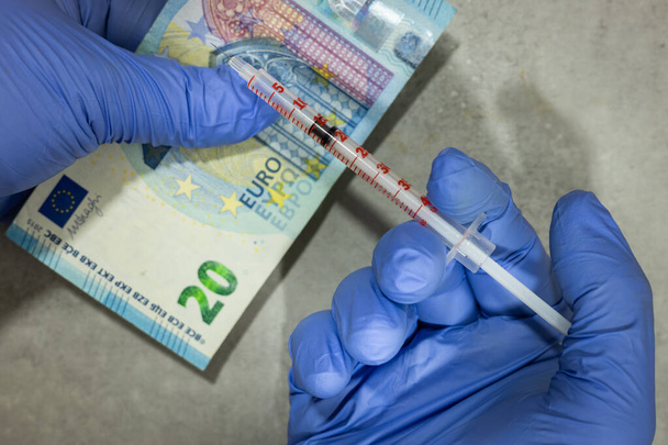Náklady na očkování a výzkum nové varianty omicronu, konceptu, přijímače v laboratorních rukavicích s 20 eurobankovkou a injekční stříkačkou s injekcí  - Fotografie, Obrázek