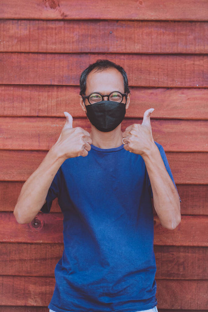 アジアの男は顔保護マスクをつけて親指のサインを上げる - 写真・画像