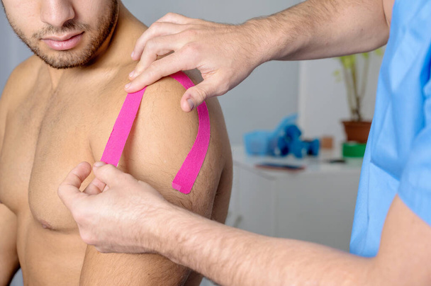 Physical therapist applying kinesio tape on male patient shoulder. Kinesiology, physical therapy, rehabilitation concept. close up - Φωτογραφία, εικόνα