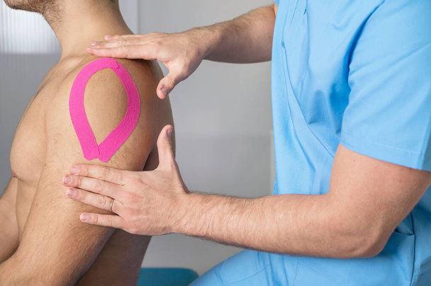 Physical therapist applying kinesio tape on male patient shoulder. Kinesiology, physical therapy, rehabilitation concept. close up - Fotografie, Obrázek