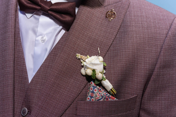 Männliche Boutonniere junge mit Hahnenfuß auf einem braunen Anzug in den Strahlen des warmen Lichts. Konzept von jung, Familie, Hochzeit. Selektiver Fokus  - Foto, Bild
