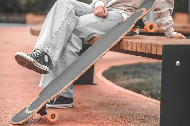 Legs near skateboard of person sitting in park - Photo, Image