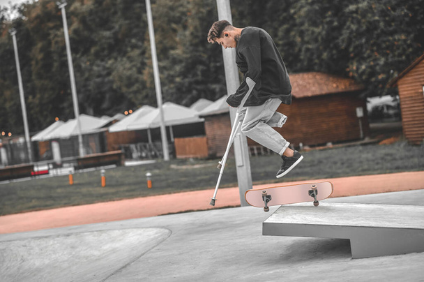 Guy on crutches while jumping on skateboard from springboard - Foto, imagen