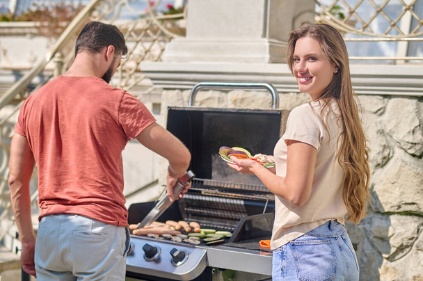A man in red shirt standing near the barbecue grill and cooking veggies - Foto, Imagen