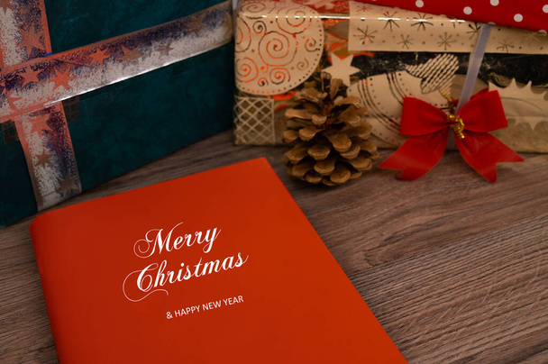 Boek met "Merry Christmas" op de cover op een houten tafel met kerstcadeaus op de achtergrond. - Foto, afbeelding