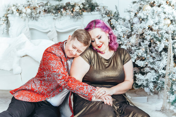 LGBTQ lesbijska para świętuje Boże Narodzenie lub Nowy Rok zimowe wakacje razem. gej kobieta kobieta z męski partner przytulanie podłogi w domu. Zimowy nastrój świąteczny. Para zakochanych - Zdjęcie, obraz