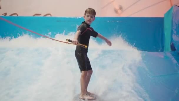 Child and instructor at Flow Rider indoor surfing training session. Teenager on water board training on simulator wave indoors. Young surfer during training on generated waves. Water sports - Footage, Video