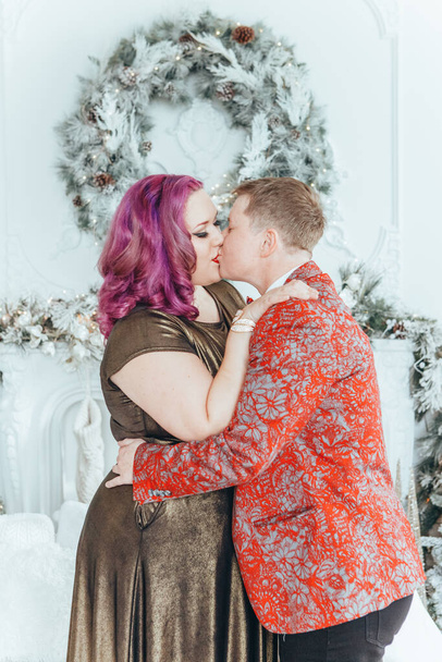 LGBTQ lesbian couple celebrating Christmas or New Year winter holiday together. Gay female lady with butch partner hugging cuddling on couch sofa at home. Winter holiday mood spirit. Couple in love. - Photo, Image