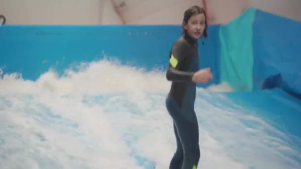Водный спорт, концепция баланса. Маленький спортсмен наслаждается серфингом в помещении. Подросток катается на доске по волнам на тренажере в спортивном комплексе. Тренер по серфингу и студент в сессии на волновом тренажере - Кадры, видео