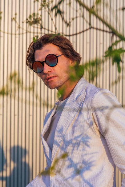 Close up portrait of a handsome man with round hippie sunglasses during sunset - Фото, изображение
