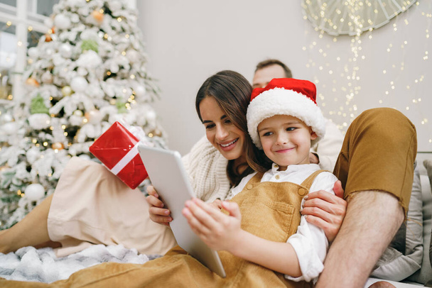 Ευτυχισμένη οικογένεια που διασκεδάζει στο ψηφιακό tablet στο κρεβάτι τα Χριστούγεννα - Φωτογραφία, εικόνα