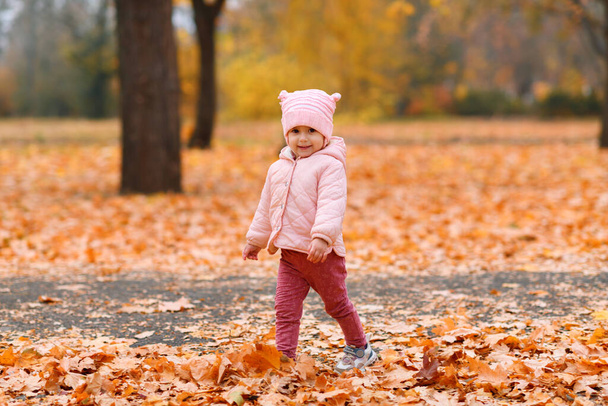 Дитяча дівчинка гуляє в осінньому міському парку. Красива природа, дерева з жовтим листям
. - Фото, зображення