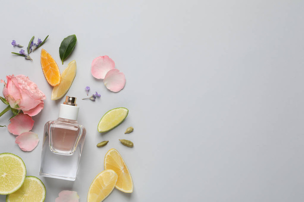 Flat lay composition with bottle of perfume and fresh citrus fruits on light grey background. Space for text - Valokuva, kuva
