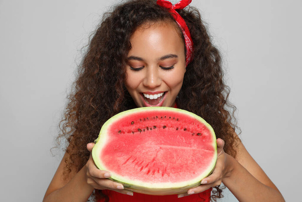 Beautiful young African American woman with half of watermelon on grey background - Foto, immagini