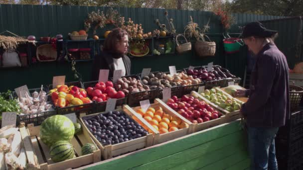 Obst auf dem Markt kaufen. Ein Mann wählt auf einem Bauernmarkt Äpfel und Melonen aus. Hinter dem Tresen steht eine Verkäuferin. - Filmmaterial, Video