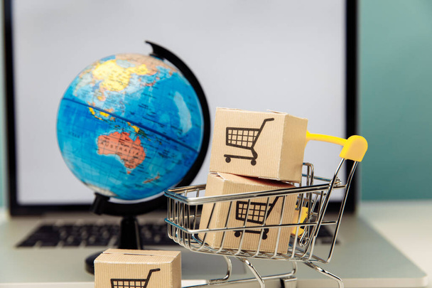 Καλάθι αγορών Globe και σούπερ μάρκετ με κουτιά σε φόντο laptop. Έννοια online αγορών. - Φωτογραφία, εικόνα