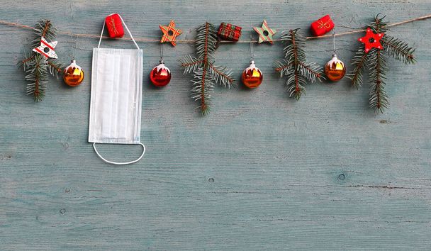 Κορόνα και Χριστούγεννα. Μια προστατευτική μάσκα κρέμεται δίπλα σε μπάλες χριστουγεννιάτικου δέντρου, κλαδιά ελάτης και πακέτα δώρων - Φωτογραφία, εικόνα