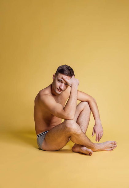 One young handsome shirtless brown-eyed man sitting on floor isolated on yellow studio background. Natural beauty concept - Φωτογραφία, εικόνα