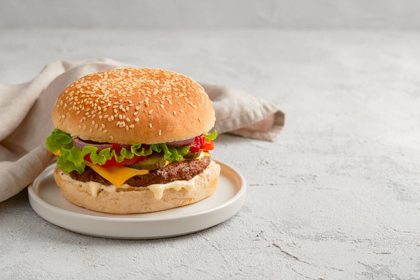 Classic traditional cheeseburger with beef, tomato, lettuce, pickles and onion on gray background - Photo, Image