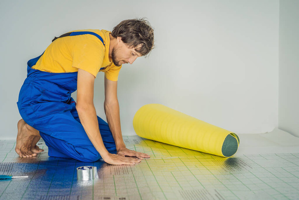 Master installs the overlapping thermal insulation in the room. Floor heating installation. Male hand holds reinforced tape. Repair in the apartment, floor insulation - Foto, imagen